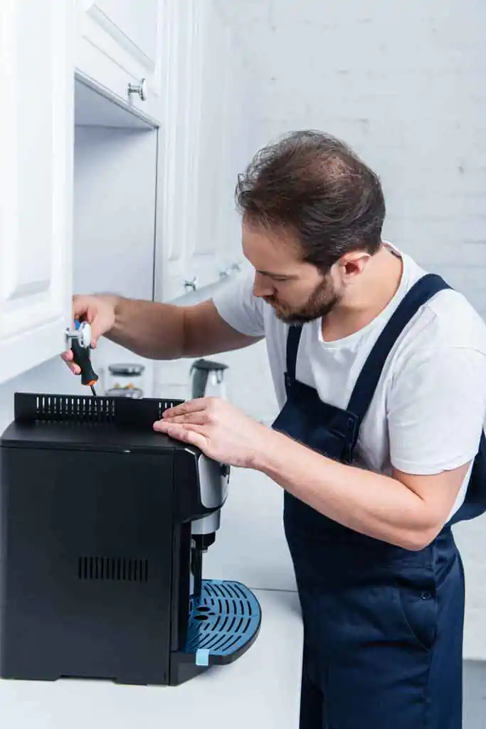 Adult handyman at general work repairing the coffee machine with a screwdriver in the kitchen